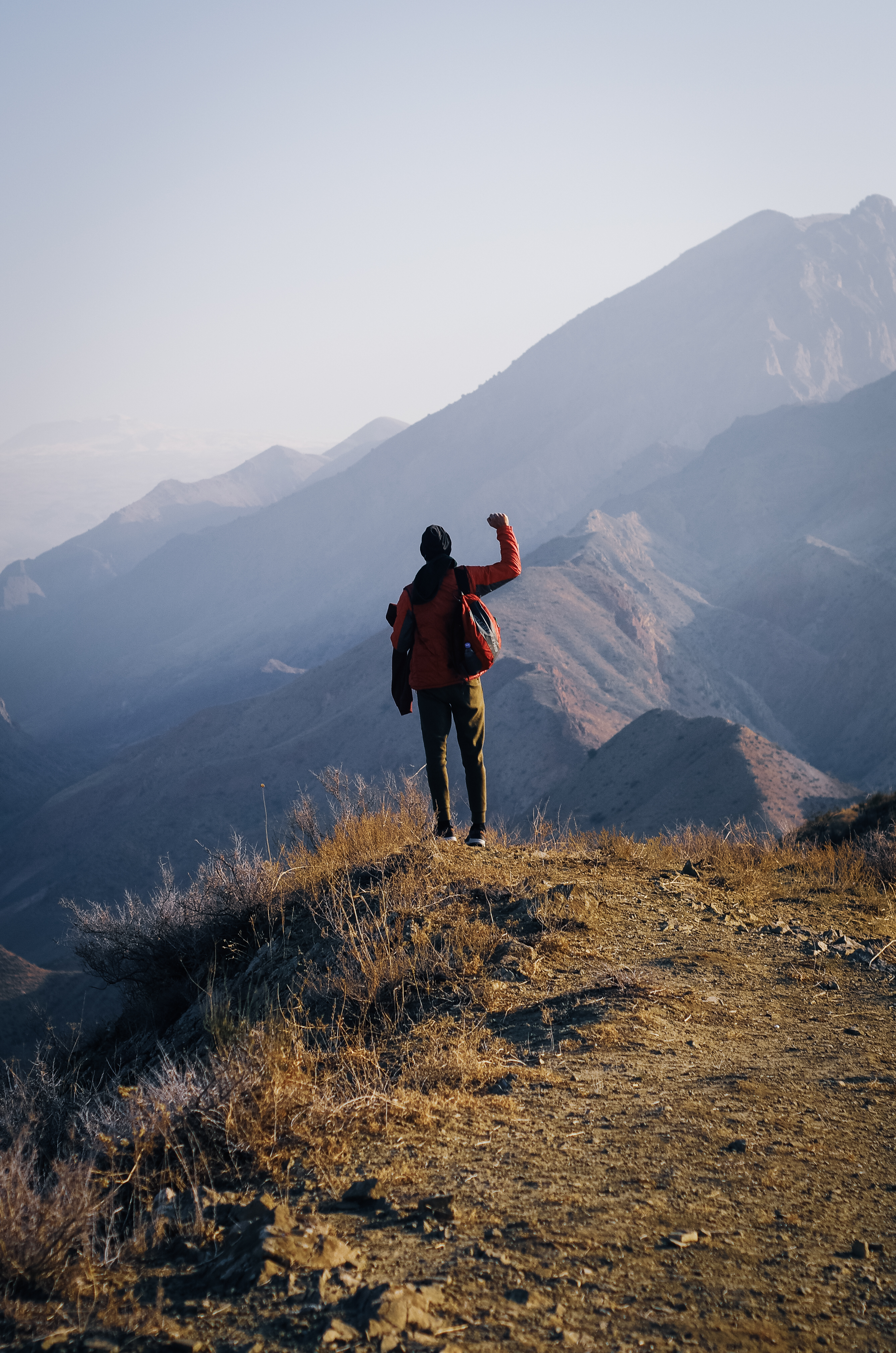 A lone hiker signaling from a ridge above layered Armenian mountains